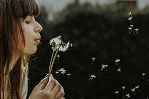Woman blowing dandelion seeds from a flower